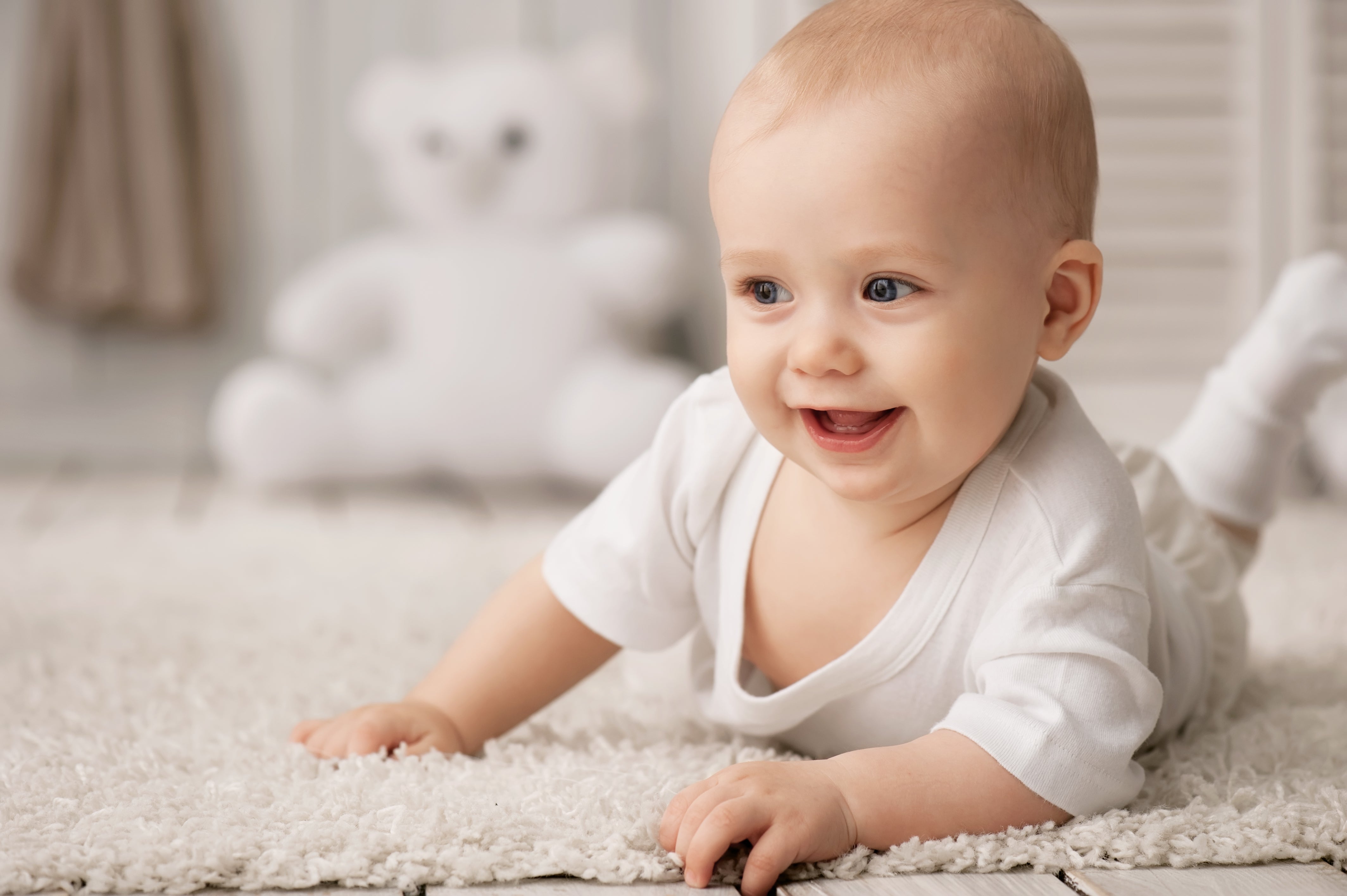 Baby with big smile laying on his stomach on a carpet